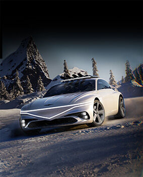 The Genesis X Snow Speedium Concept vehicle is dynamically driving over a white snowfield, with a coniferous forest in the background. It features two rows of front lights: one horizontal and the other forming a V-shape, both glowing white.